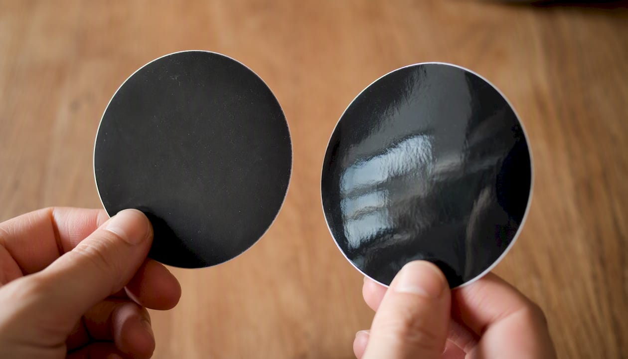 Hands holding matte and glossy stickers side by side