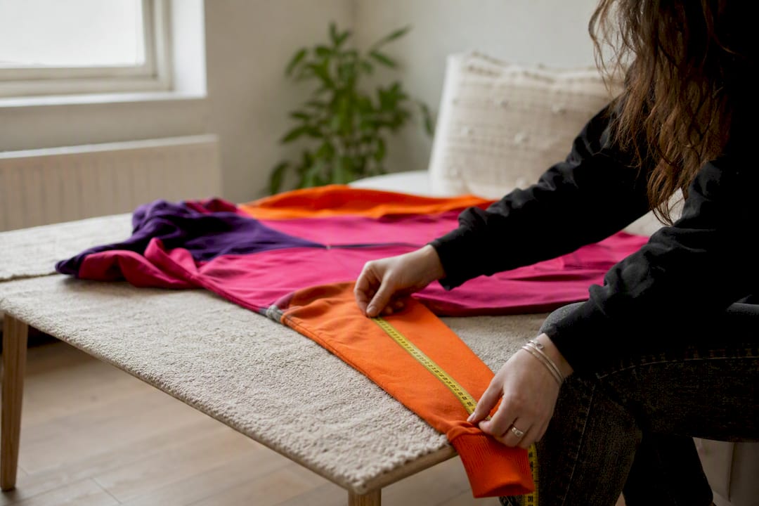 Hands measuring hoodie flat on table
